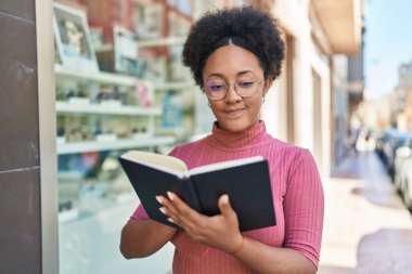 Afro-Amerikalı kadın gülerek sokakta kendine güvenen kitap okuyor.