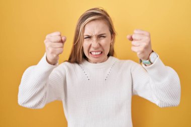 Beyaz süveter giyen genç beyaz bir kadın. Kızgın ve kızgın. Öfkeyle bağırırken kızgın yumruklar sallıyor. öfke ve agresif konsept. 