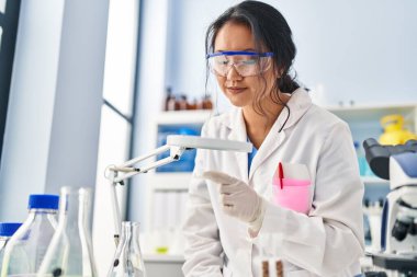 Young chinese woman wearing scientist uniform using loupe at laboratory
