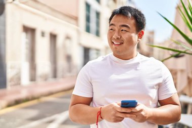 Young chinese man smiling confident using smartphone at street