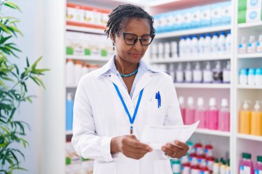 Orta yaşlı Afro-Amerikan kadın eczacı eczanede reçete okuyor.