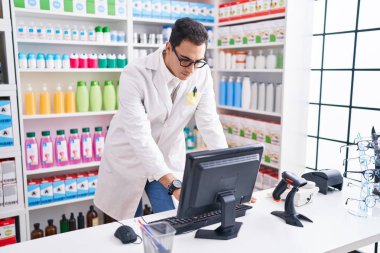 Young hispanic man pharmacist using computer at pharmacy