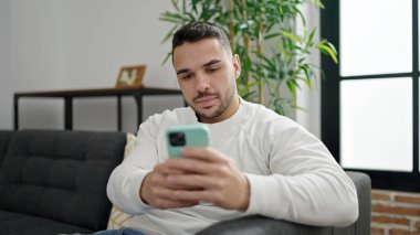 Evdeki kanepede oturan, akıllı telefon kullanan genç bir İspanyol.