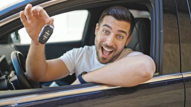 Young hispanic man smiling confident holding key of new car at street