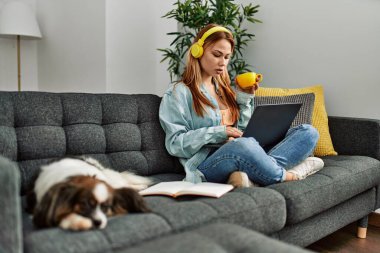 Kanepede oturan beyaz bir kadın ve evde ders çalışan bir köpek.