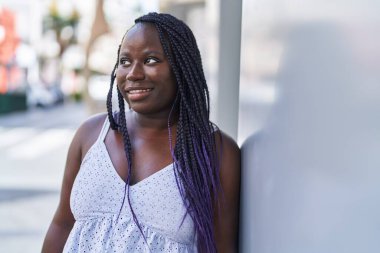 Afro-Amerikalı kadın gülümsüyor. Kendinden emin bir şekilde caddeye bakıyor.