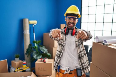 Evde çalışan, sakallı, genç, İspanyol bir adam. Seni ve kamerayı işaret ediyor. 