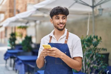 Young arab man waiter using smartphone working at restaurant