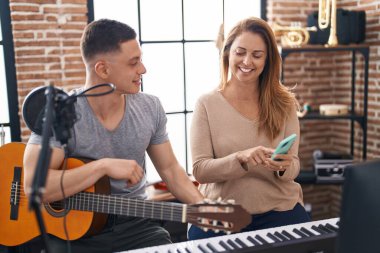 Man and woman musicians having classic guitar lesson using smartphone at music studio