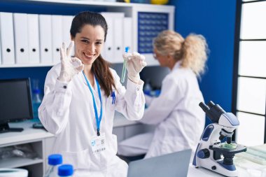 Laboratuvarda çalışan Latin asıllı genç bir kadın parmaklarıyla imza atıyor, gülümseyerek mükemmel bir sembol oluşturuyor. 