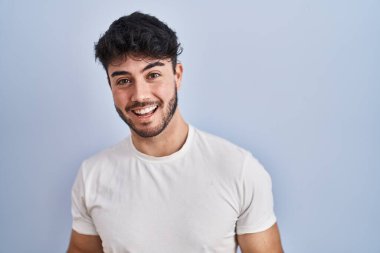 Hispanic man with beard standing over white background smiling cheerful with open arms as friendly welcome, positive and confident greetings 