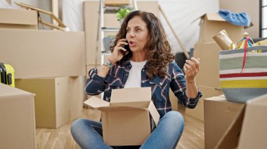 Orta yaşlı İspanyol kadın telefonda konuşuyor. Yeni evdeki karton kutuları açıyor.