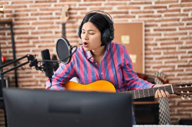 Young chinese woman musician playing guitar at music studio