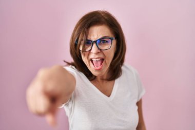 Orta yaşlı İspanyol kadın pembe arka planda dikiliyor. Kameraya kızgın ve sinirli olduğunu gösteriyor. 