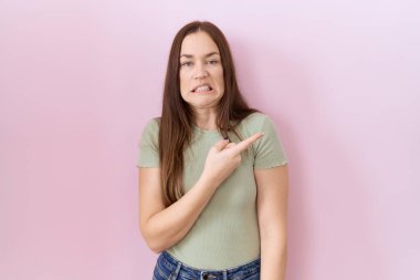 Güzel esmer kadın pembe arka planda dikiliyor endişeli ve endişeli bir şekilde işaret ediyor. 