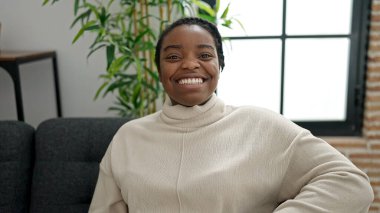 Afro-amerikalı bir kadın evdeki koltukta kendinden emin bir şekilde oturuyor.