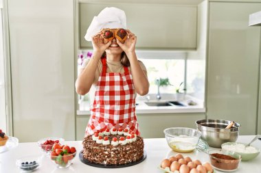 Genç ve güzel İspanyol kadın gülümsüyor. Mutfakta keklerini gözünün üstünde tutuyor.