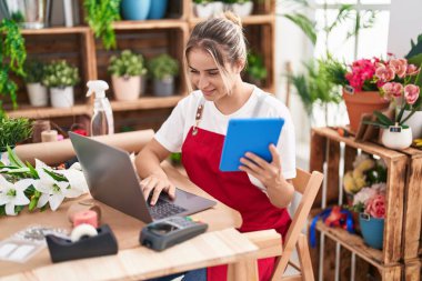 Young blonde woman florist smiling confident using laptop and touchpad at flower shop