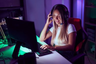 Young beautiful hispanic woman streamer playing video game using computer at gaming room