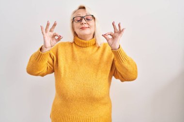 Orta yaşlı beyaz kadın arka planda duran gözlüklü rahat ve gözleri kapalı meditasyon yaparken parmaklarıyla gülümseyen. yoga konsepti. 
