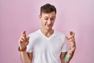 Pembe arka planda duran beyaz bir adam umut ve gözlerin kapalı bir şekilde gülümseyerek işaret ediyor. Şans ve batıl inançlar. 