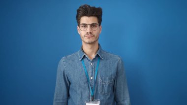 İzole edilmiş mavi arka planda gevşek bir ifadeyle duran İspanyol genç adam.