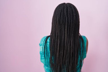 Pembe arka planda duran ve kollarını kavuşturup arkaya bakan genç Afro-Amerikalı. 