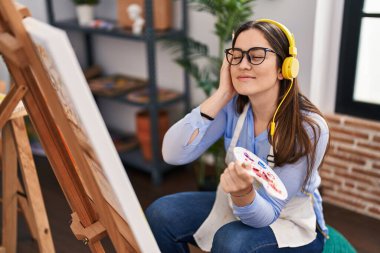 Sanat stüdyosunda müzik dinleyen genç bir kadın sanatçı.