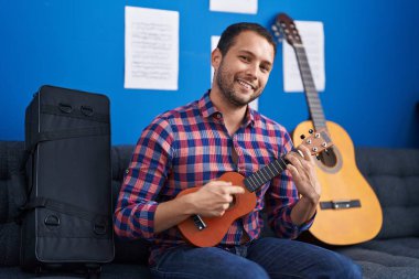 Genç müzisyen müzik stüdyosunda ukulele çalarken kendinden emin gülümsüyor.