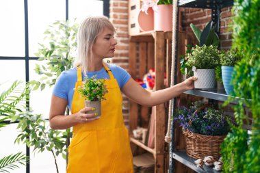Young blonde woman florist holding plant at florist