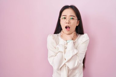 Pembe arka planda duran genç Çinli kadın boğularak can çekiştiği için bağırıyor ve boğuluyor. Sağlık problemi. Boğulma ve intihar konsepti. 