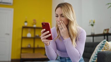 Genç, güzel, İspanyol bir kadın akıllı telefon kullanıyor. Evde üzgün görünüyor.