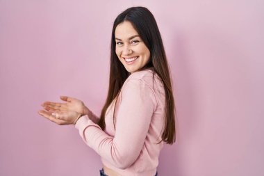 Pembe arka planda duran genç esmer kadın avuçlarını açıp fotokopi alanını gösteriyor, gülümseyerek mutlu bir şekilde gülümsüyor. 