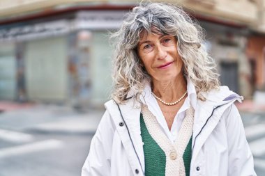 Orta yaşlı bir kadın sokakta kendine güvenerek gülümsüyor.