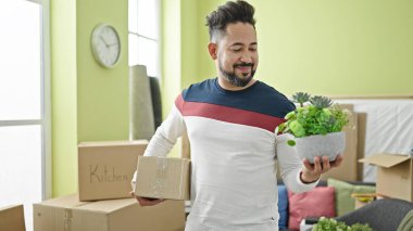 Genç Latin adam gülümsüyor. Kendine güveni tam. Paket ve bitki yeni evinde.
