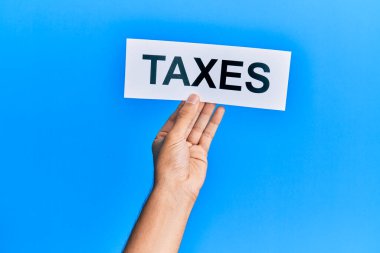 Elinde vergi sözcüğüyle izole edilmiş mavi arka planı olan beyaz bir adamın eli.