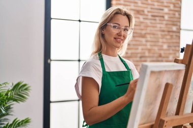 Sanat stüdyosunda kendine güvenen genç sarışın sanatçı gülümsüyor.