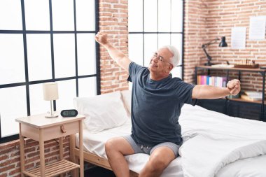 Middle age grey-haired man waking up stretching arms at bedroom