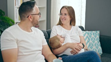 Anne, baba ve bebeğin ailesi evdeki kanepede otururken gülümsüyor.