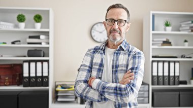 Orta yaşlı bir iş adamı, kollarını çapraz yapıp ofiste ciddi bir ifade takınıyor.