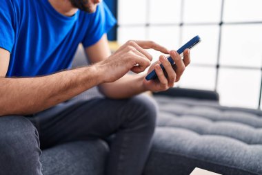 Genç adam evde koltukta oturan smartphone kullanarak