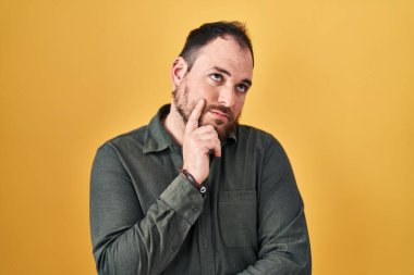 Ayrıca sarı arka planda sakallı, eli çenesinde soru soran, düşünceli bir İspanyol. Düşünceli bir yüzle gülümsüyor. şüphe kavramı. 