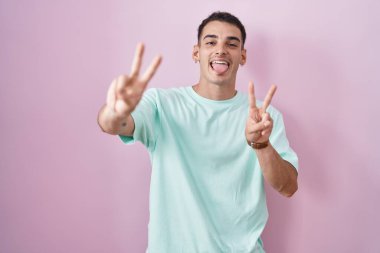 Pembe arka planda dikilen yakışıklı İspanyol adam iki elini de göstererek gülümseyerek zafer işareti yapıyor. İki numara.. 