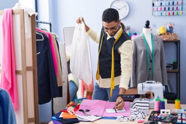 Genç Arap terzi gülümsüyor. Giysi fabrikasında not defterine tişörtü tutuyor.