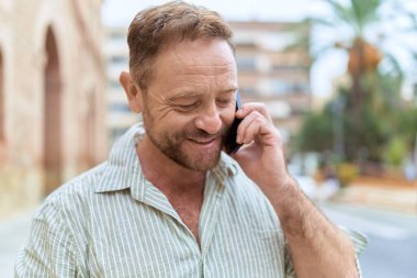 Orta yaşlı bir adam gülümsüyor. Sokakta akıllı telefondan konuşuyor.