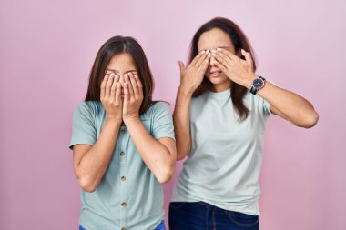 Pembe arka planda duran genç anne ve kız yorgunluk ve baş ağrısı, uykulu ve yorgun yüz ifadeleri için gözlerini ovuşturuyorlar. görme sorunu 