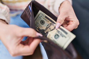 Young caucasian woman holding wallet with dollars sitting on sofa at home