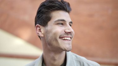 Young hispanic man smiling confident looking to the side at street
