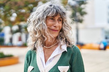 Orta yaşlı bir kadın parkta kendine güvenerek gülümsüyor.