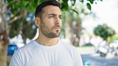 Genç İspanyol bir adam parkta ciddi bir ifadeyle yan tarafa bakıyor.